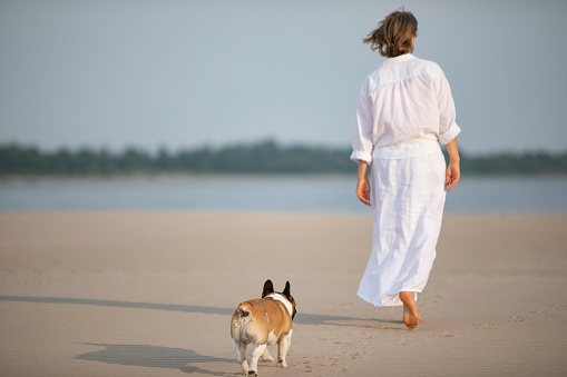 Young adult woman walking with her French bulldog at the beach