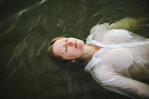 Young woman in white dress lying down in the water