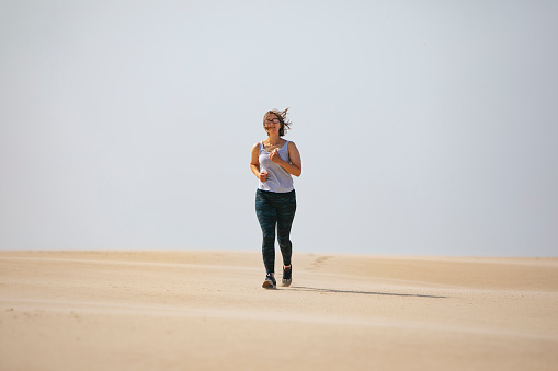 Young adult woman jogging in sand dunes