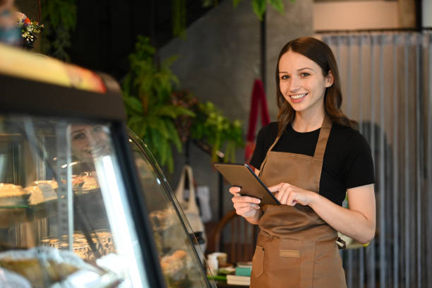 istock Smiling caucasian woman small business owner using digital tablet while standing in front of showcase in coffee shop. 1456995646