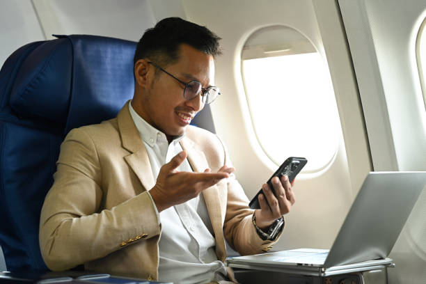 istock Handsome businessman in formal clothes using mobile phone while sitting in airplane cabin near window. 1457001844