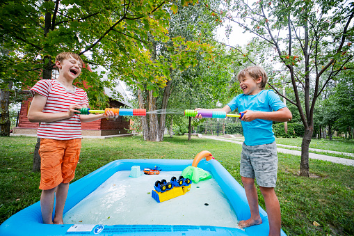 Two brothers playing with toy water guns at back yard