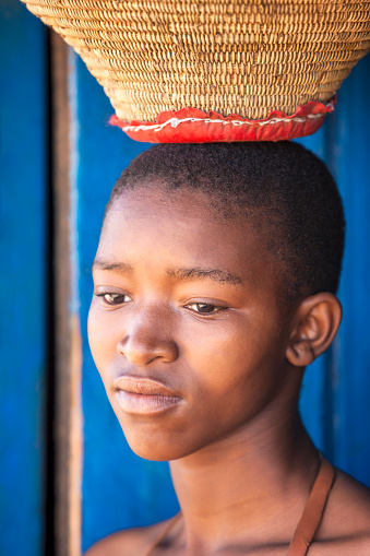 young african girl with a leather traditional costume carry a weaved basked on her head, village in botswana