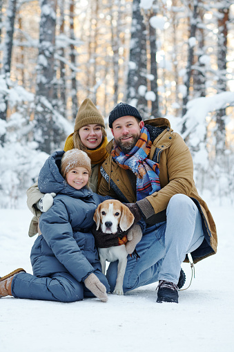 Portrait of happy family smiling at camera while walking with dog in winter forest