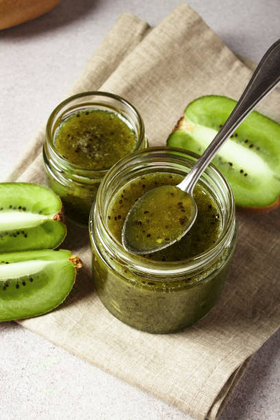 Homemade kiwi jam in a jar and kiwi slyces on concrete background with copy space