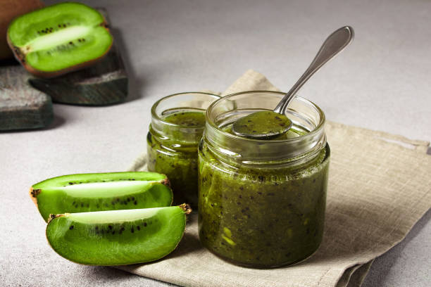 Homemade kiwi jam in a jar and kiwi slyces on concrete background with copy space