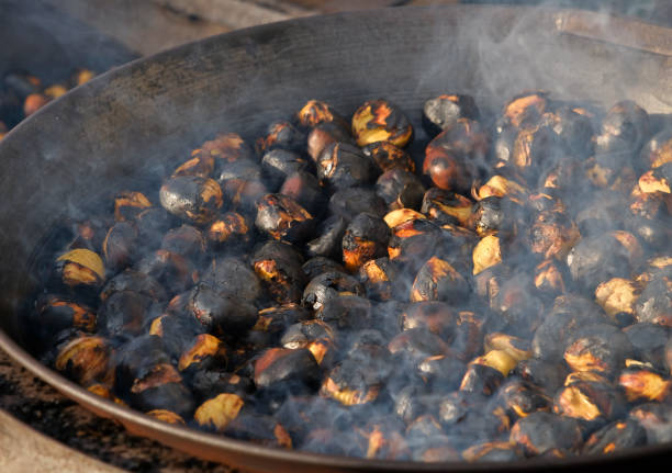 typical for south tyrol, in the iron pan over the open fire roasted chestnuts (also called "keschtn"). these can be bought at market stalls in the autumn and winter months. - bressanone imagens e fotografias de stock