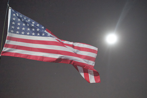 American flag blowing in the wind on a starry full moon night