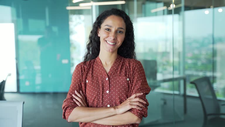 Portrait of happy beautiful hispanic young woman creative employee looking at camera and smiling in modern office