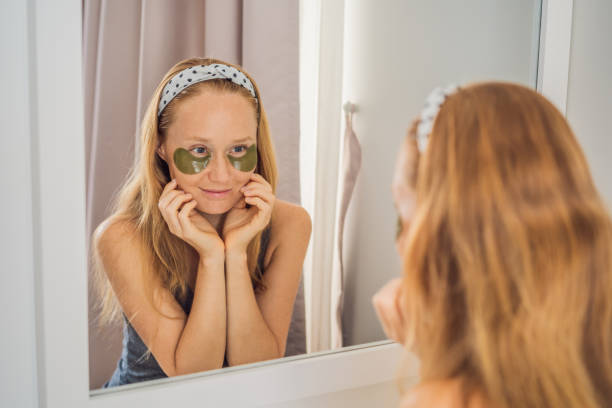 istock Mirror reflection smiling woman applying hydrogel eye care patches, moisturizing skin under eyes, enjoying skincare procedures 1457017778