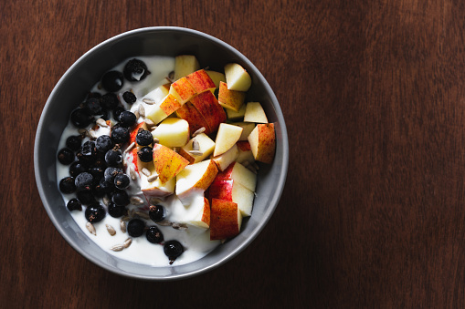Healthy fruit and yogurt breakfast bowl on a wooden surface with slices of apple, blackcurrants and sunflower seeds. Top view, copy space.