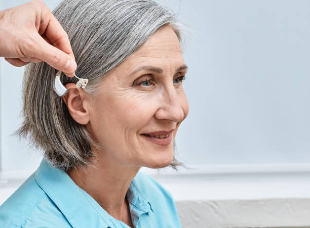 istock Installation hearing aid on senior woman's ear at audiology center, close-up, side view. Deafness treatment, hearing solutions 1457023568