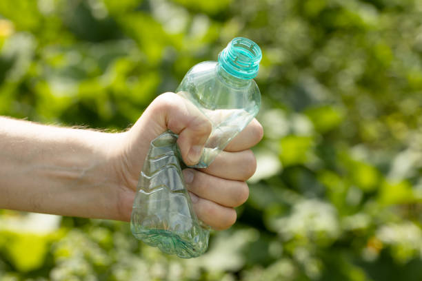 Hand holding crumpled empty plastic bottle in the park. High quality photo