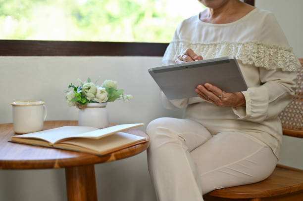 istock cropped image, 60s aged Asian woman sitting by the window and using portable digital tablet. 1457030841