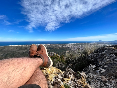 POV Point of view shot of a young hiker sport male having fun and relaxing after hiking a mountain sitting over the top seeing all the landscape include the mediterranean sea and Valencia City, Spain.
