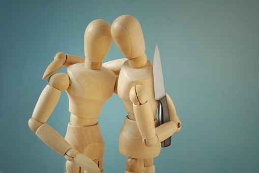Wooden mannequins hugging each other with knife behind back - Concept of betrayal and disloyalty