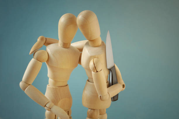 Wooden mannequins hugging each other with knife behind back - Concept of betrayal and disloyalty stock photo