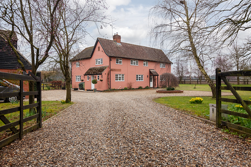 Cromwell Cottage, Kennett, Suffolk, England - March 1 2019: Substantial detached cottage within landscaped gardens with rendered facade painted in traditional 'suffolk pink' occupying generous landscaped gardens viewed from the public highway.