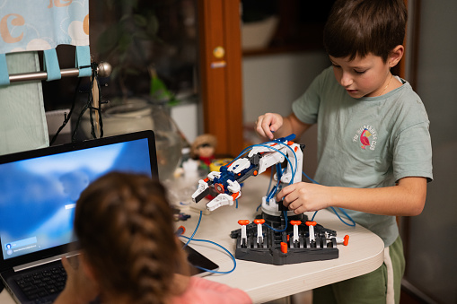 Children learning repairing getting lesson control robot arm, robotic machine arm in home workshop, technology future science education.
