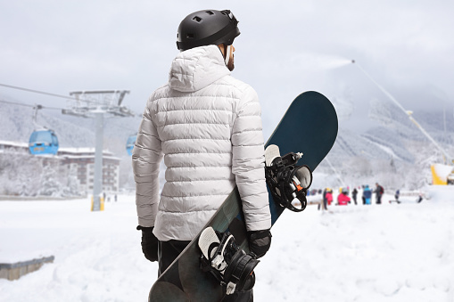 Rear view shot of a man with a snowboard looking at a ski resort