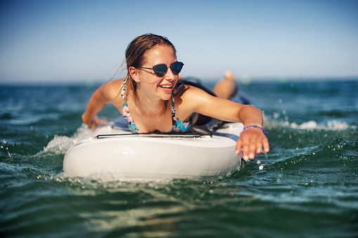 Teenage girl enjoying summer vacations. The girl is enjoying SUP paddleboard on the sea.\nCanon R5
