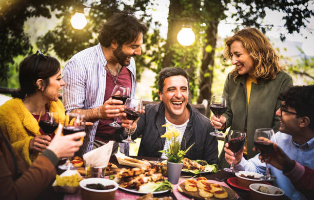 Young men and women having fun drinking out at wine diner - Food and beverage life style concept on mixed age people enjoying time together at villa patio - Warm filter with bulb string lights halo stock photo