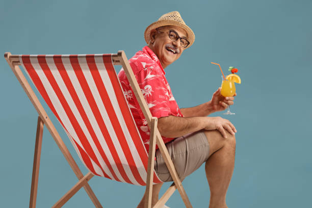 Turista maschio maturo seduto su una sedia sorridente e holdoing un cocktail - foto stock