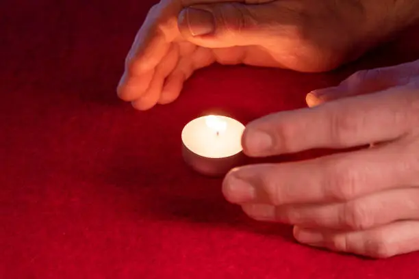 Hands warming themselves on a tealight, red background. High quality photo