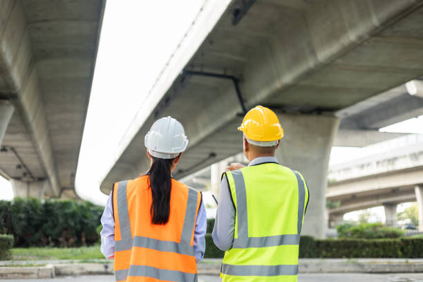 istock Two Asian worker engineer man and woman architect looking construction with white safety helmet in construction site. Standing at highway concrete road site. Work planning with blueprint and tablet. 1457050667