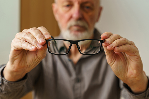 Close up of male hands holding a pair of glasses. Man's face out of focus.