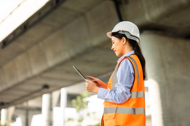 istock Asian engineer worker woman or architect looking construction with tablet wear white safety helmet in construction site. Standing at highway concrete road site. Progress planning of highway bridge. 1457051060