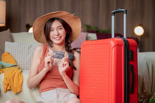 Asian traveller Tourist woman casual cloth in hotel room making credit card reservation for flight while she is unpacking suitcase with pleasure and cheerful