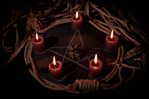 Voodoo doll, black candles, pentagram and old books on witch table. Occult, esoteric, divination and wicca concept. Mystic, voodoo and vintage background