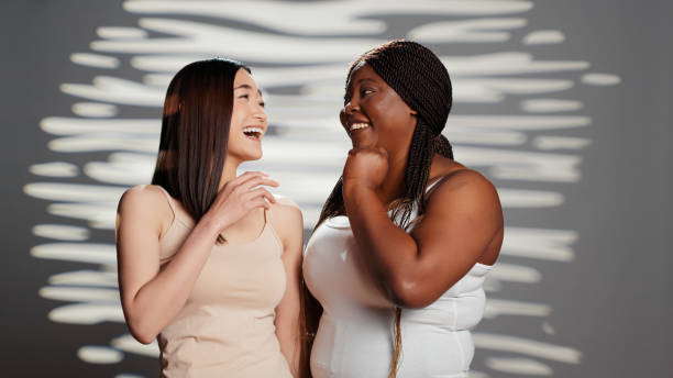 Curvy young adult telling secret to asian lady on camera Curvy young adult telling secret to asian lady on camera, acting sensual and positive in studio. Diverse beauty models advertising body positivity and self confidence, having fun. plus size woman fashion laughing stock pictures, royalty-free photos & images