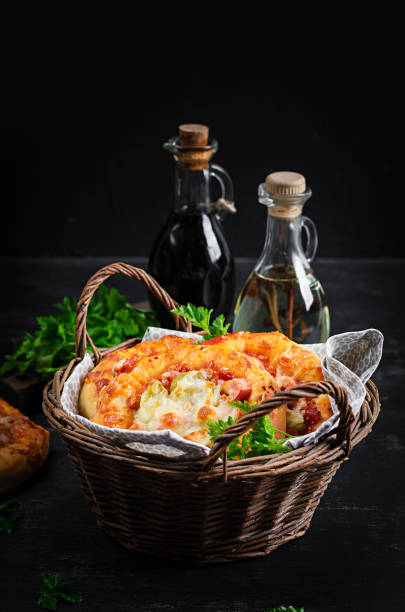 Children mini pizza , small open pies with ham, tomato sauce, mozzarella and cheese in basket on a dark background.