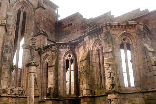 Santo Domingo gothic style convent and church ruins, close-up view of building exterior , cruceiro stone cross and apse with pointed windows. Founded around 1282. Pontevedra city, Galicia, Spain.