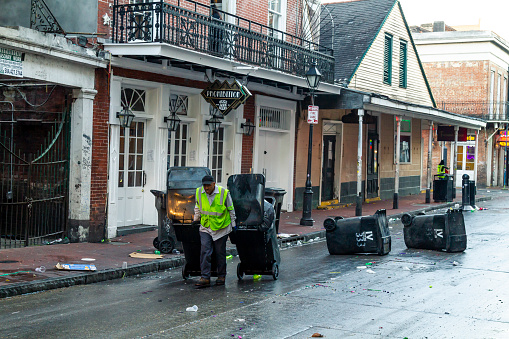 New Orleans, Louisiana, USA United States of America - March 1, 2022: A group of municipal employees working to clean and taking out thousands of tons of garbage are thrown into the streets every day in the Carnival days. Here is an example of this in the French Quarter neighborhood.\n\nThe Mardi Gras is one of the emblematic events of this city that attracts millions of nationals and internationals tourists to the city during the days of the carnival.