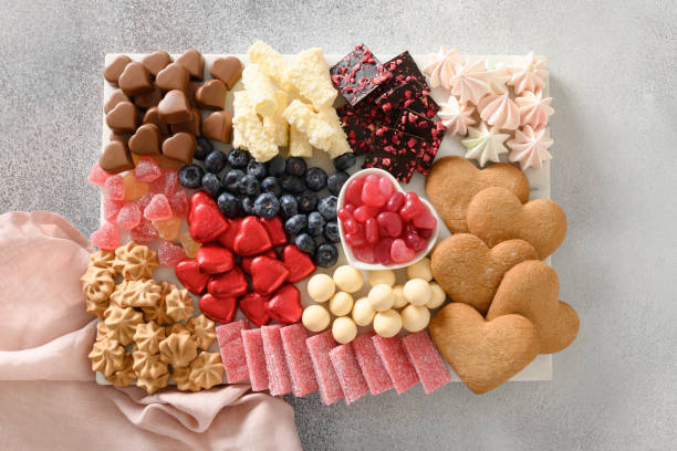 Charcuterie Valentines Day sweet board with chocolate, red hearts, different sweets, berries and candies on gray background. Top view. Romantic appetizer.
