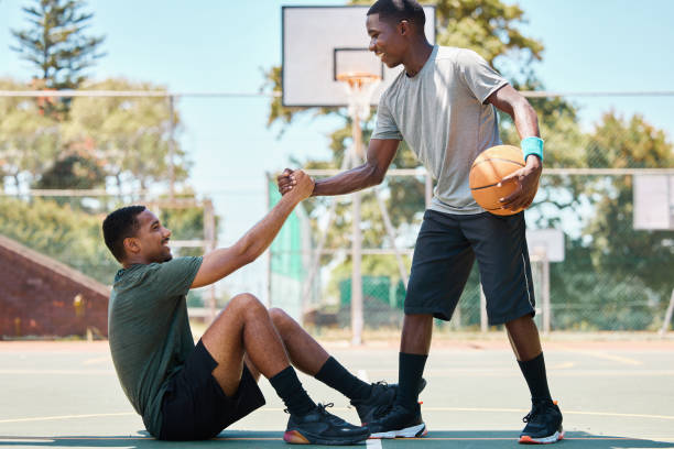 basketball, sports and teamwork, helping hand and support, respect and assistance in competition training games. happy basketball player holding hands with friend, trust and kindness on outdoor court - basketball playing ball african descent imagens e fotografias de stock