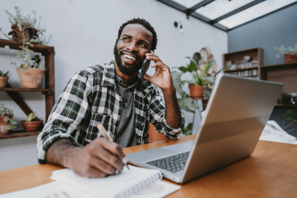 Man working from home on laptop talking on smartphone