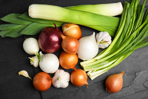 Fresh onion bulbs, leeks and garlic on black table, flat lay