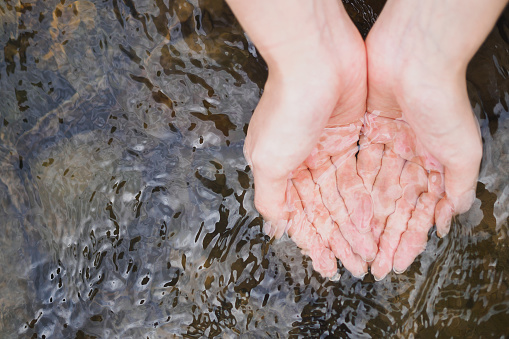 A woman's cupped hand is holding clean natural water in the river, copy space