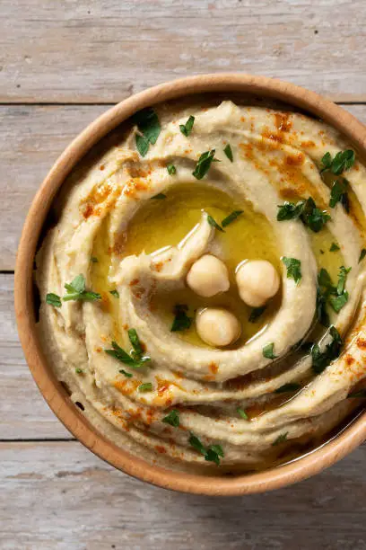 Chickpea hummus in a wooden bowl garnished with parsley, paprika and olive oil on wooden table