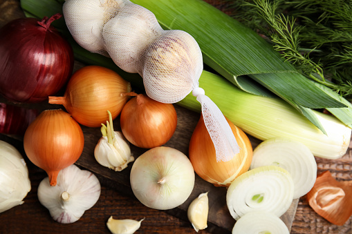 Fresh onion bulbs, leeks, garlic on wooden table, flat lay