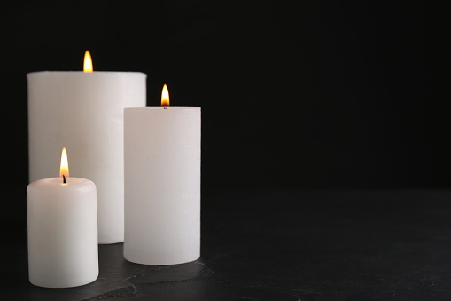 Burning candles on slate table against black background. Space for text