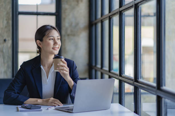 istock Asian female accountant doing calculations analyzing reports pointing at graphs holding pen using laptop placed on table at office 1457080609