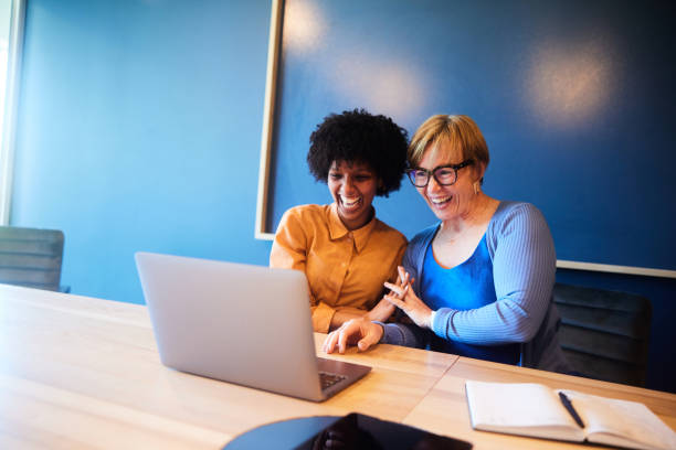 istock Diverse businesswomen laughing while working at a board room table 1457081192