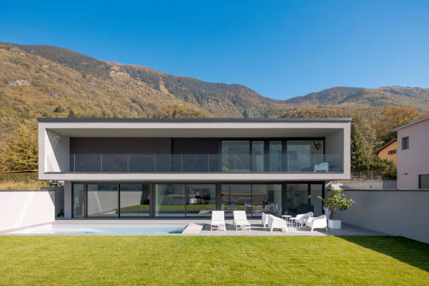 istock Front view modern house with two floors, pool two deck chairs and a small lounge with white armchairs. In front is a beautiful green lawn 1457082155