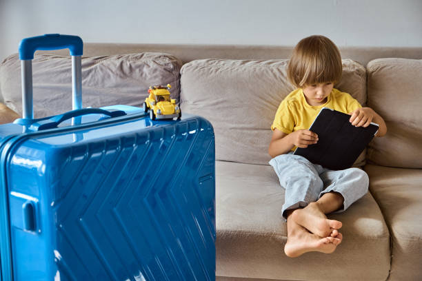 istock Child using a tablet buying online tickets or waiting for vacation at home next to a packed suitcase 1457082186