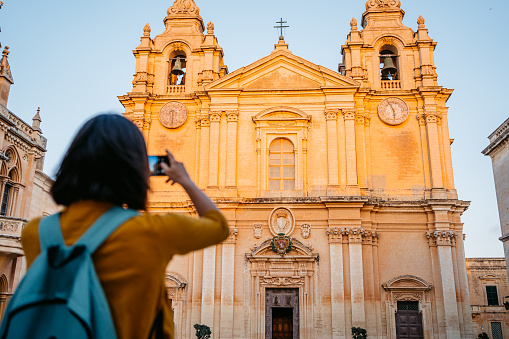 Beautiful young female tourist taking a picture using smart phone of St Paul's Cathedral in Malta.